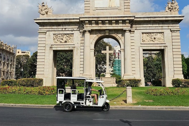 Electric cart in front of historic stone arch with decorative carvings on a sunny day.