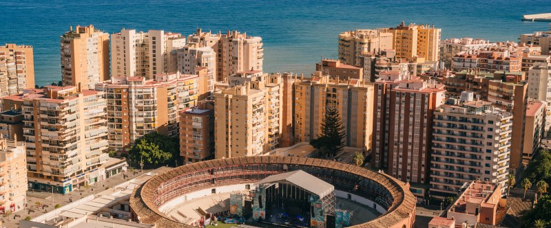 Aerial view of a seaside city with a circular stadium surrounded by tall buildings.