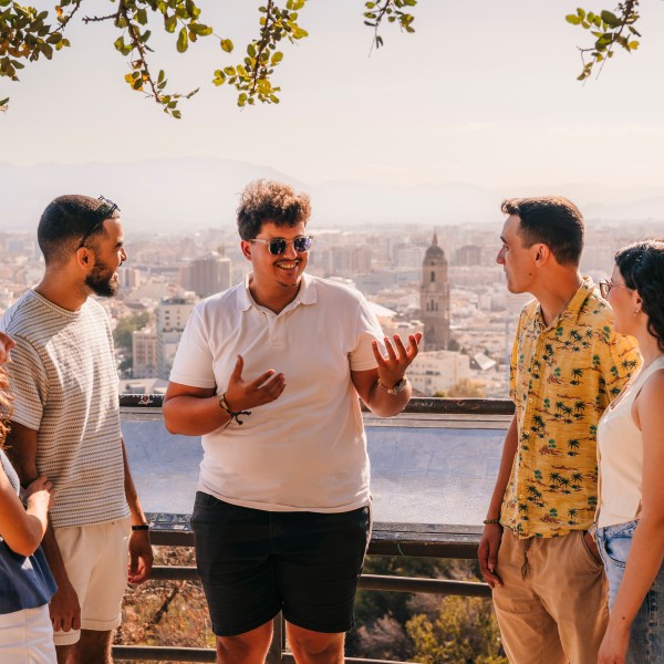Five people chatting on a scenic viewpoint overlooking a city with distant mountains.