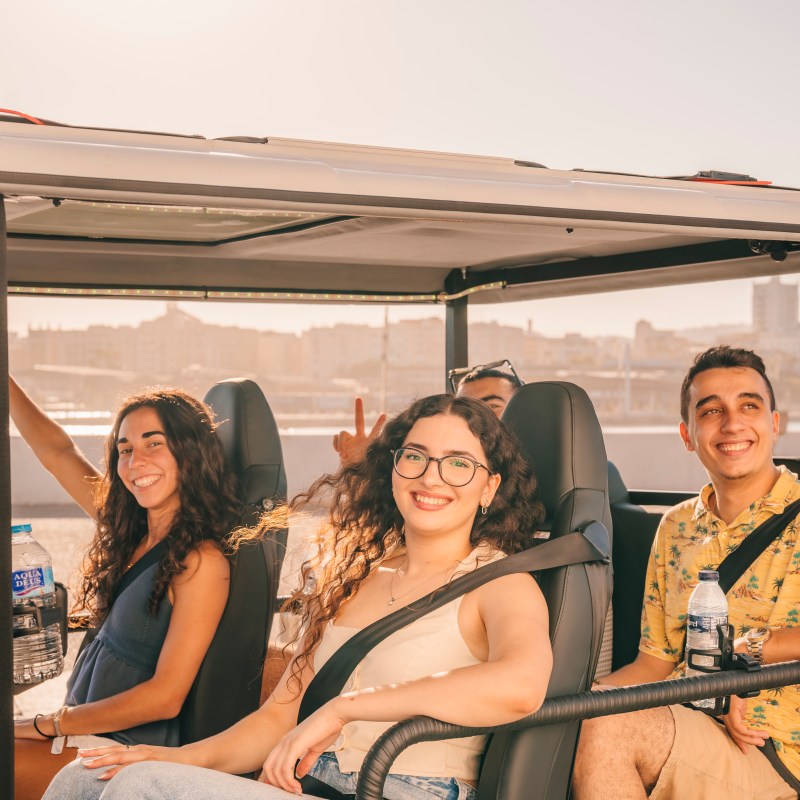 Three people smiling inside a open-top vehicle on a sunny day.