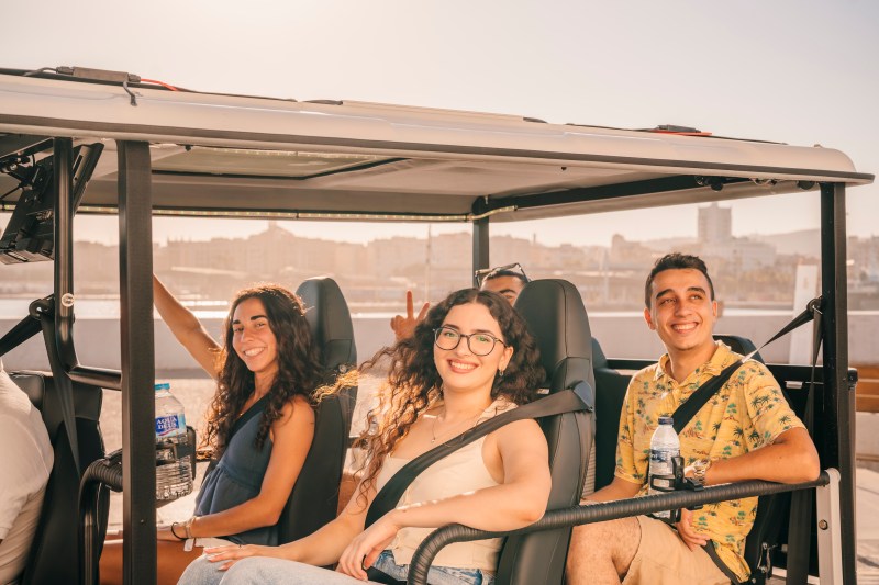Three people smiling inside a open-top vehicle on a sunny day.
