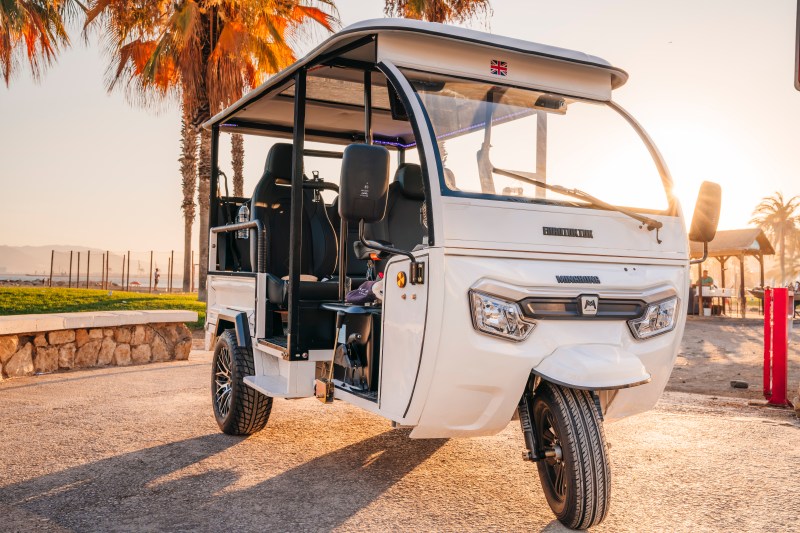 White open-sided auto rickshaw parked under palm trees at sunset.