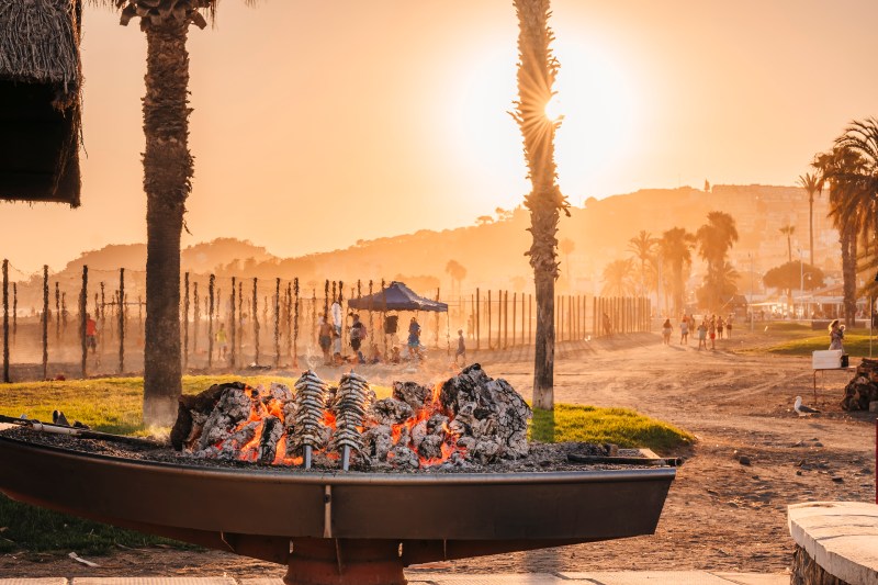 Beachside barbecue at sunset with grilling sardines and palm trees.