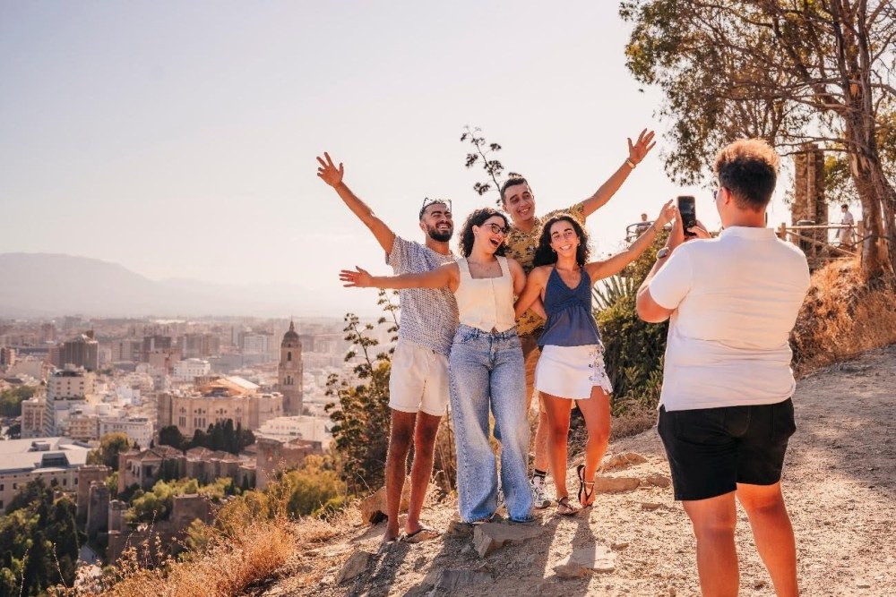 Grupo de turistas posando felices para una foto en el mirador de Gibralfaro con vistas panorámicas a la Catedral de Málaga y el centro histórico.
