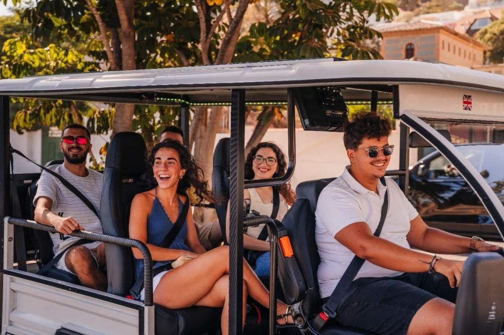 Grupo de amigos riendo y disfrutando de un tour privado por Málaga en un tuk-tuk eléctrico descapotable con conductor.